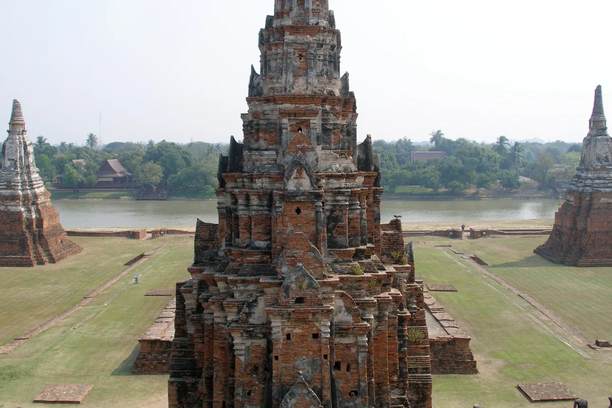 A tall Khmer-style prang towers over the ruins of Wat Chaiwatthanaram beside a river in Ayutthaya.