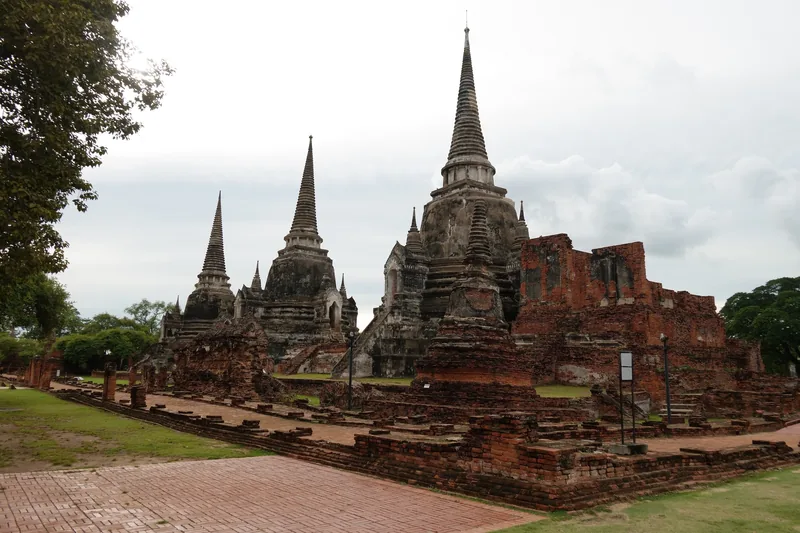 Three ancient stone chedis stand amid brick ruins at Wat Phra Si Sanphet in Ayutthaya, Thailand.