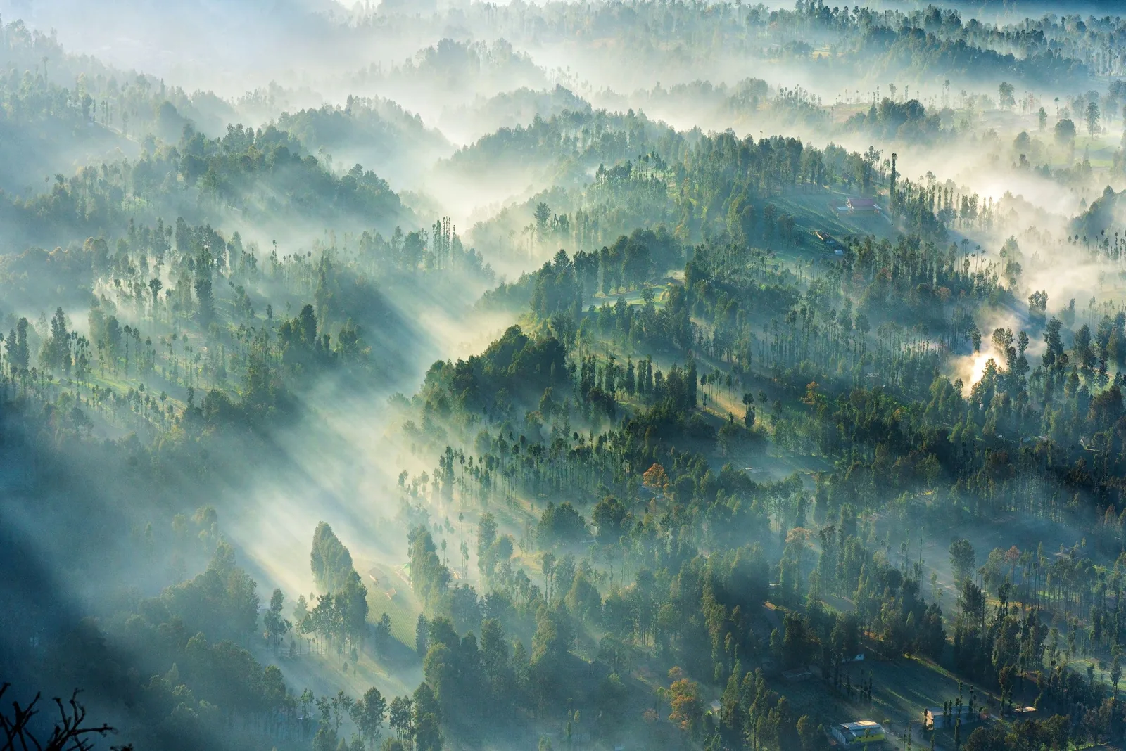 Sunbeams pierce misty forested hills in an aerial view over Java, Indonesia.