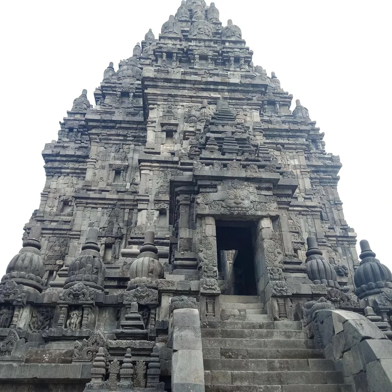 A towering stone spire with intricate carvings rises above the entrance stairway of Prambanan temple near Yogyakarta.