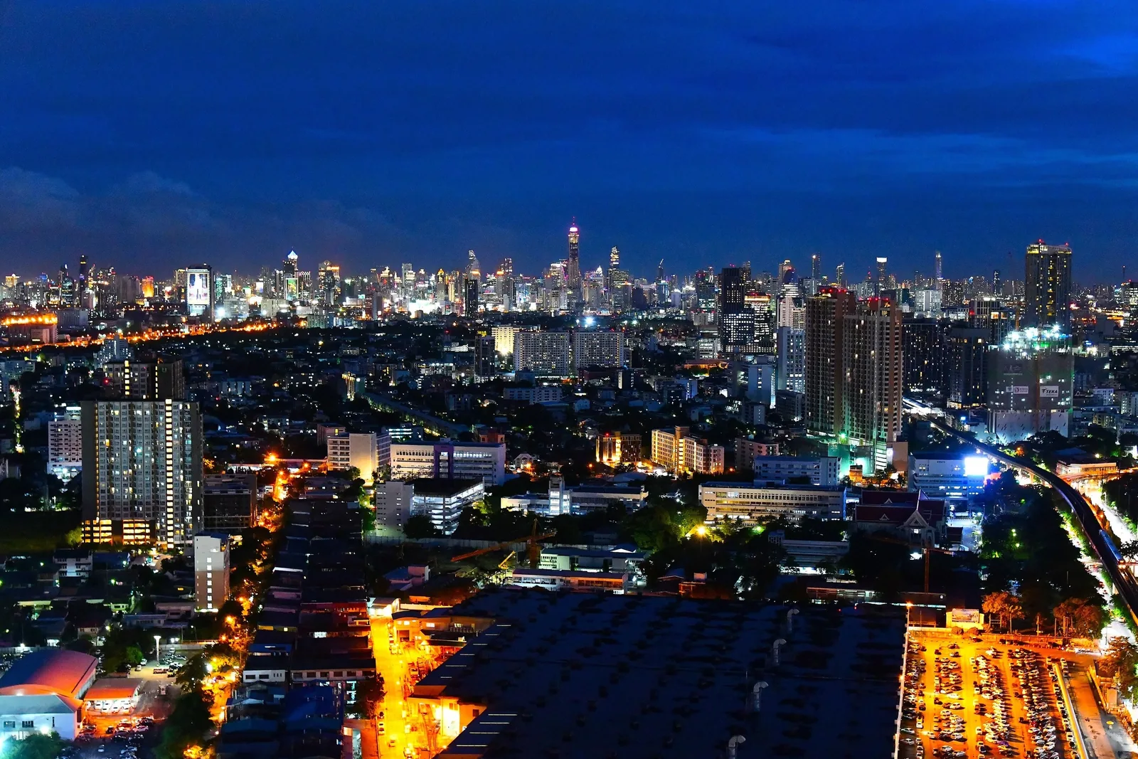Bangkok's skyline glows with illuminated skyscrapers and city streets stretching to the horizon at dusk.
