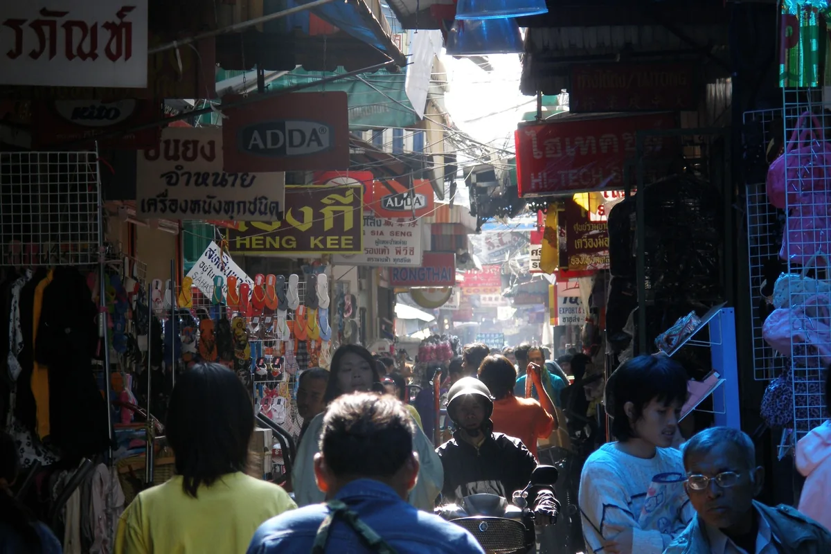 Crowded narrow alley lined with shop signs and vendor stalls in Sampeng Lane, Bangkok's Chinatown.