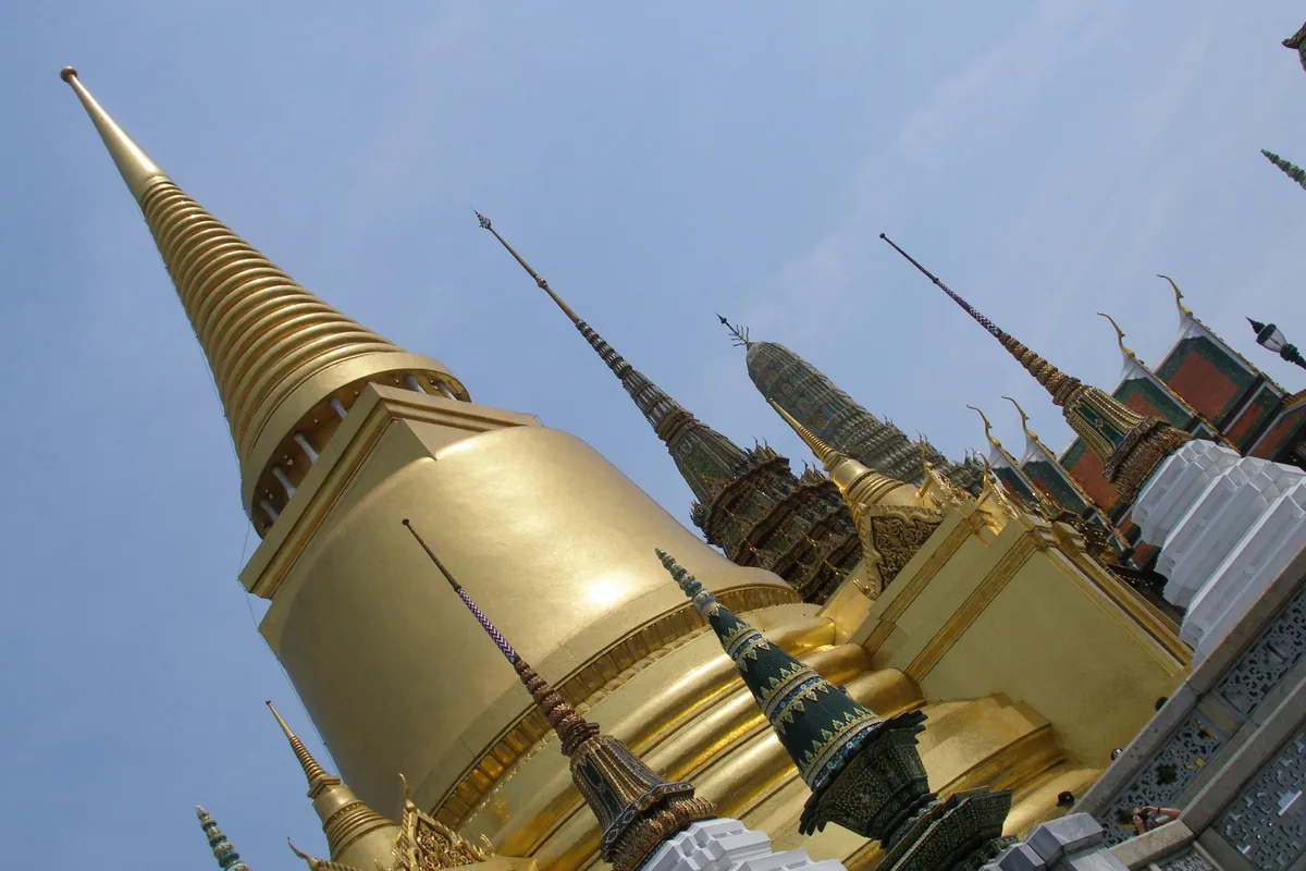 Golden chedi spire rises against a clear blue sky at Wat Phra Kaew temple complex in Bangkok.