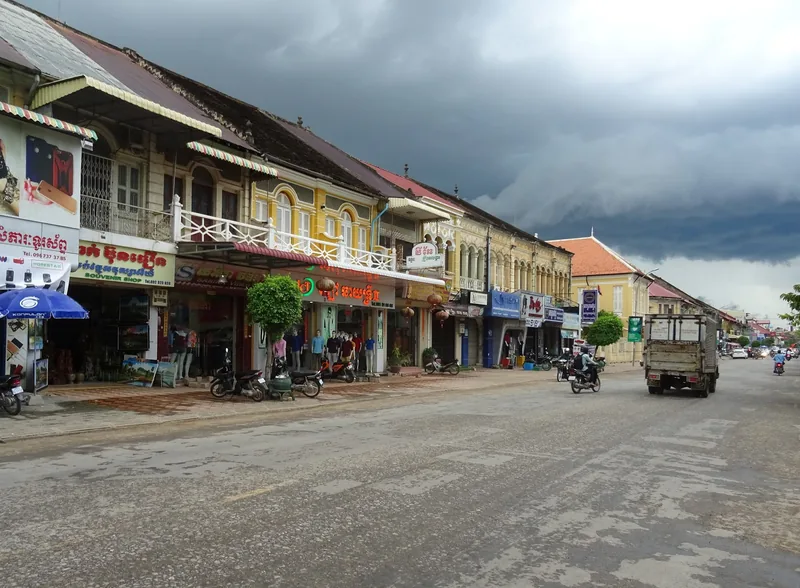 Colonial-era shophouses line a street in Battambang under a dramatic storm sky.