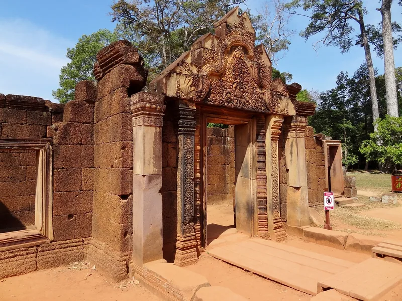An intricately carved pink sandstone gateway stands amid ruined walls at Banteay Srei temple near Siem Reap.