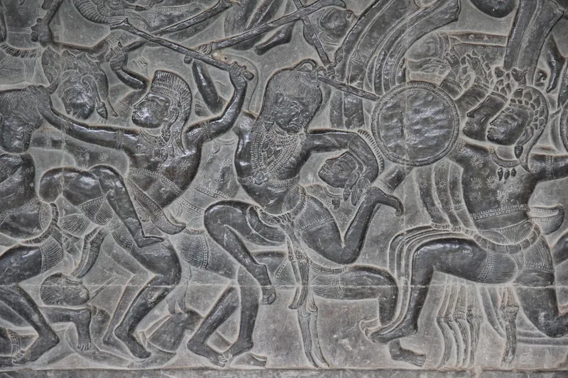 Ancient stone bas-relief depicting a battle scene with warriors, carved into a wall at Angkor Wat in Siem Reap.