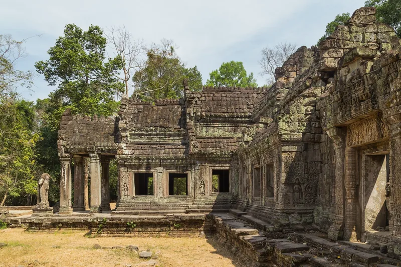 Weathered stone galleries and carved pediments stand amid trees at Preah Khan temple in Siem Reap.