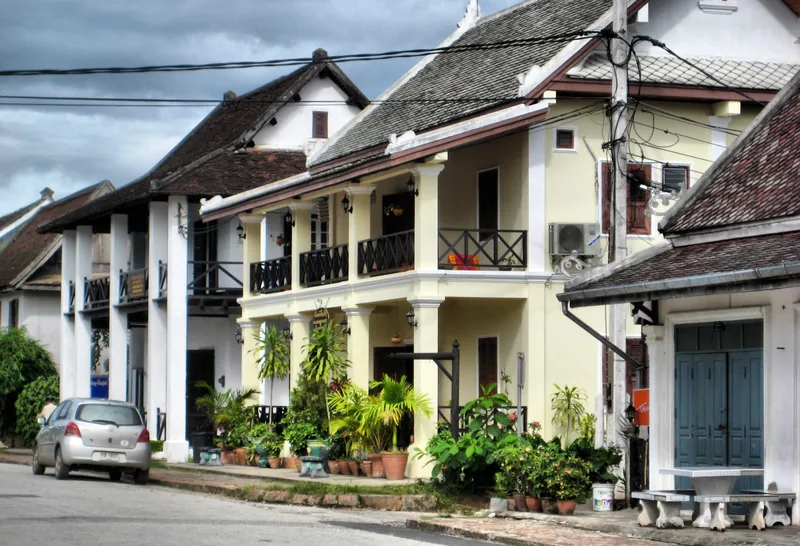 Colonial-style guesthouses with tiled roofs and balconies line a quiet street in Luang Prabang.