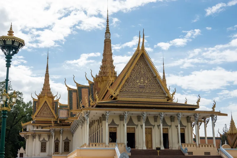 Ornate golden spires and tiered roofs crown the Throne Hall at the Royal Palace in Phnom Penh under a blue sky.