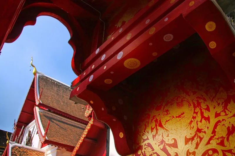 Ornate red and gold carved eaves of a temple roof against a blue sky in Chiang Mai
