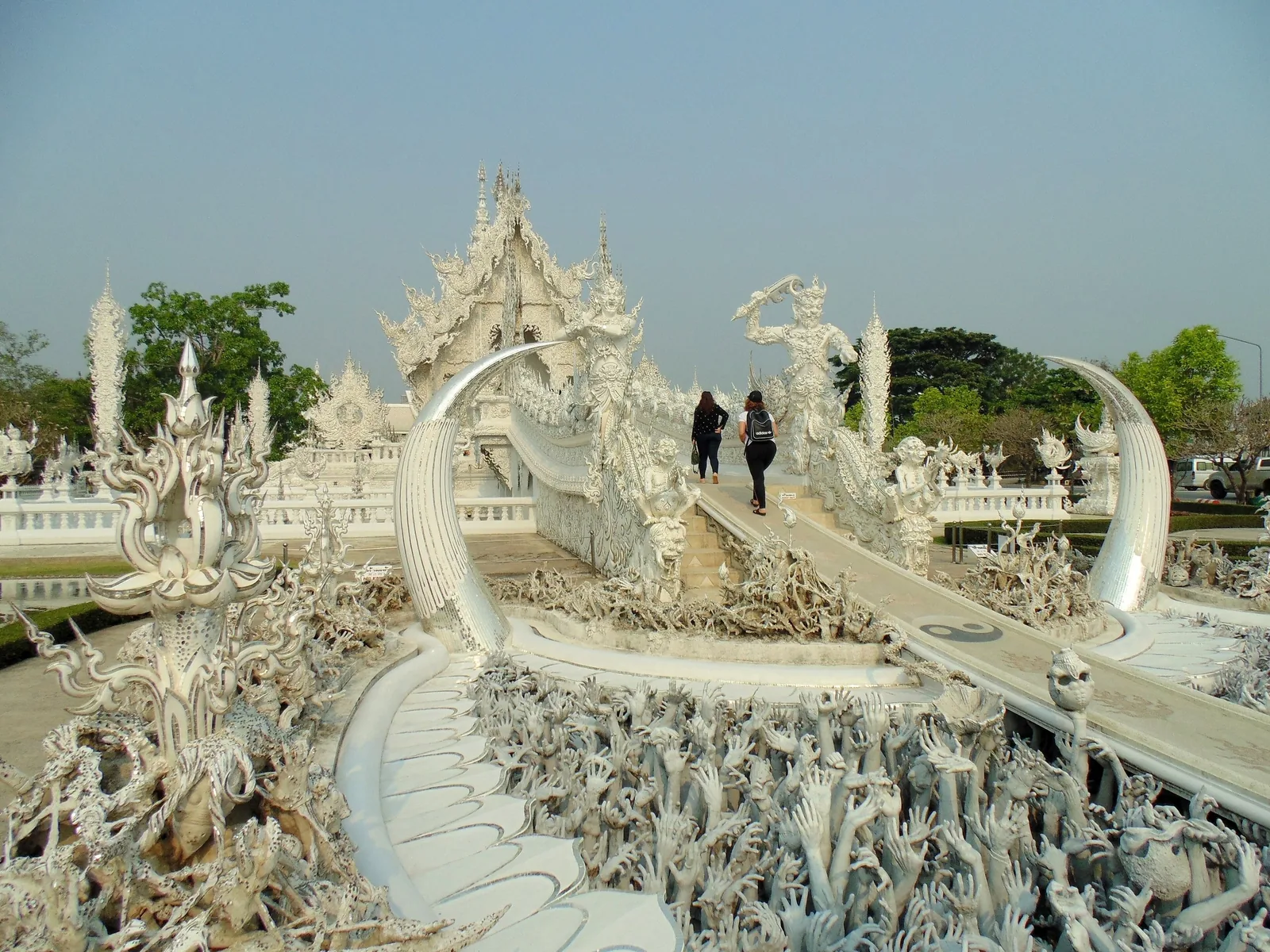 Visitors cross the ornate white bridge with sculpted hands at Wat Rong Khun temple in Chiang Rai.