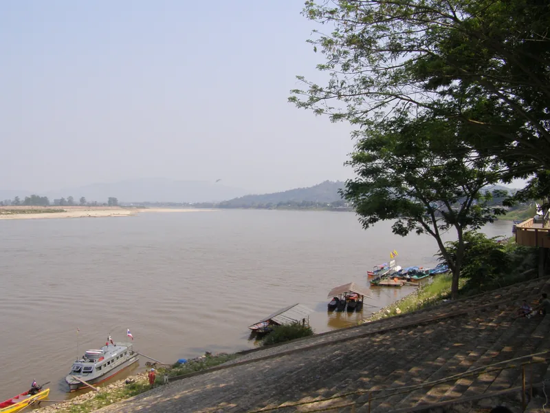 Boats moor along the Mekong riverbank near Chiang Saen in Chiang Rai under a hazy sky.