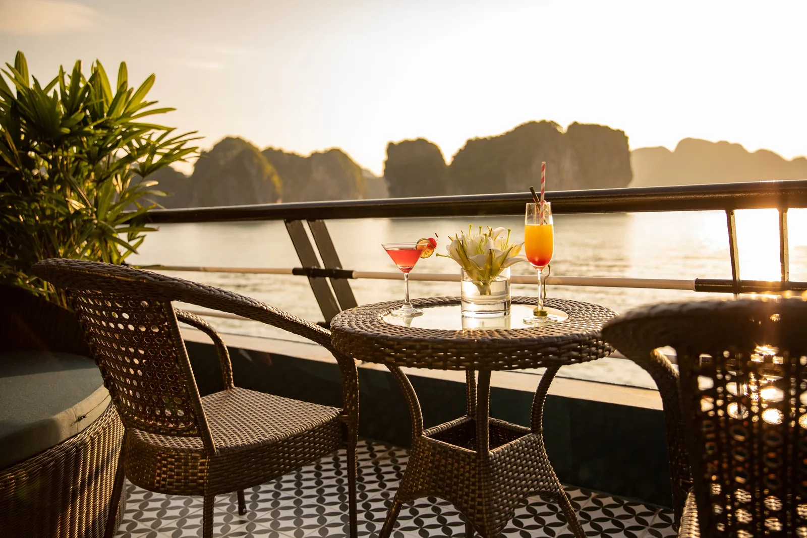 Cocktails on a table on a cruise deck overlooking Ha Long Bay's limestone karsts at sunset.