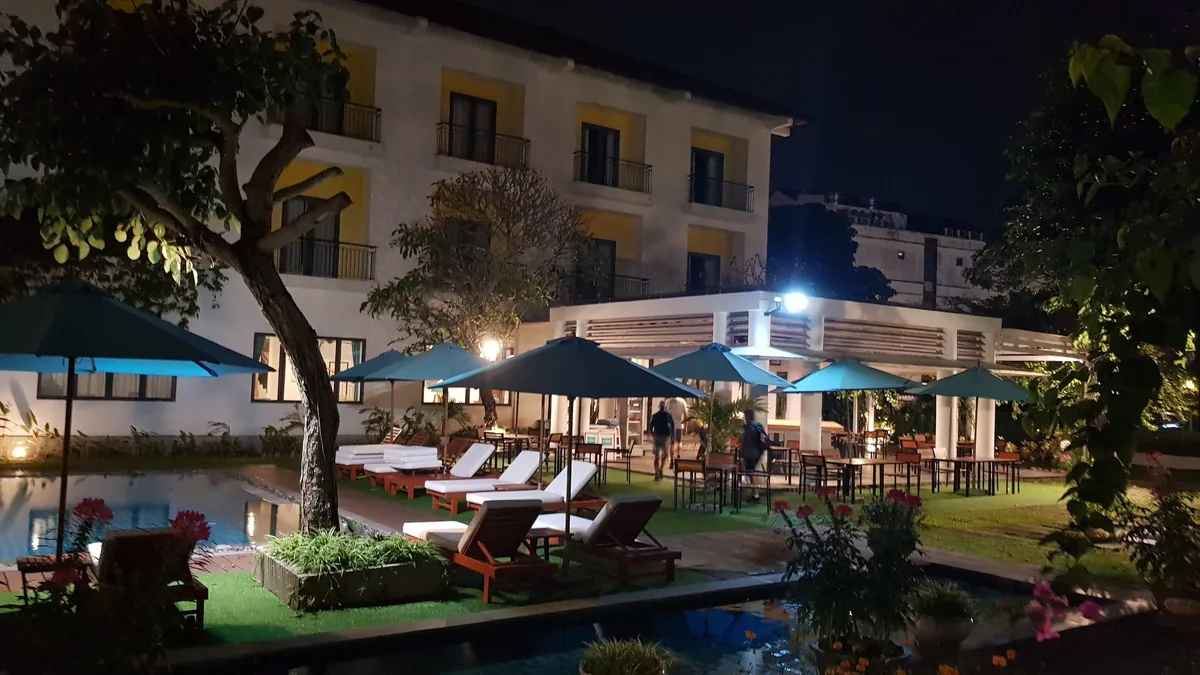 Poolside loungers and blue umbrellas glow at night beside a colonial-style hotel building in Hoi An.