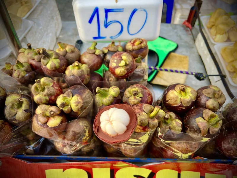 Fresh mangosteens with a price sign displayed at a market stall in Bangkok, Thailand.