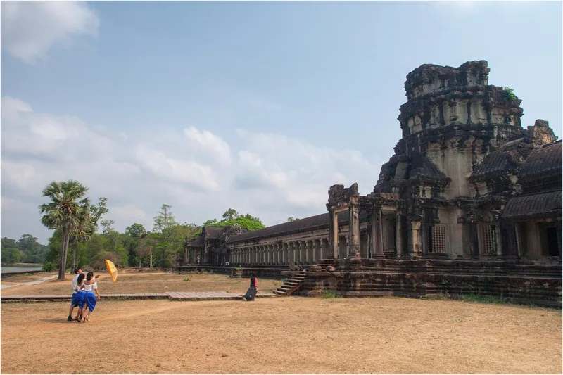 Visitors with a yellow umbrella walk beside the ancient stone galleries of Angkor Wat temple in Siem Reap.