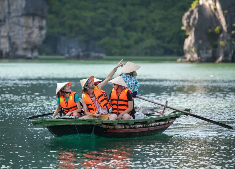 Tourists in life jackets and conical hats enjoy a rowing boat tour among limestone karsts on a cruise excursion in Vietnam.
