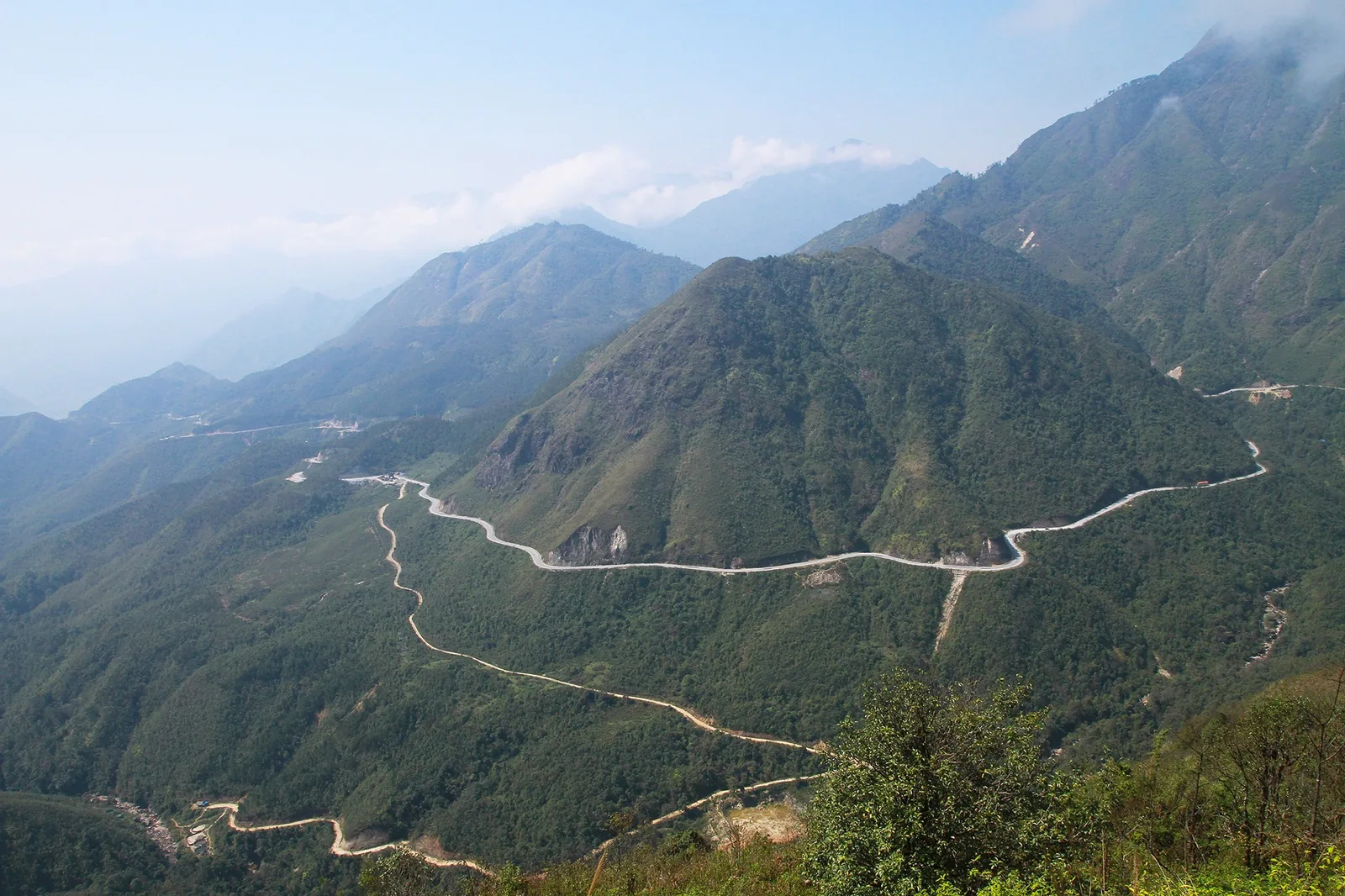 A winding mountain road snakes through green forested peaks near Sapa, Lao Cai.