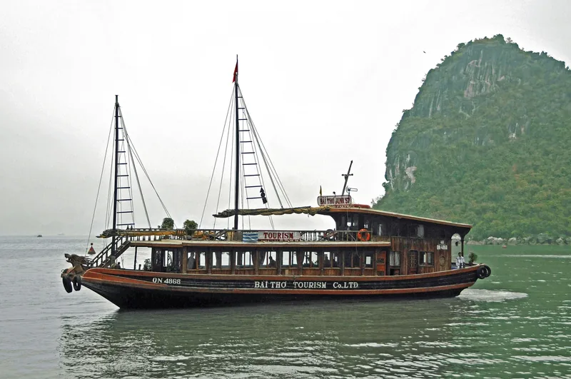 A wooden tourist junk boat cruises past a limestone karst island in Ha Long Bay, Vietnam.