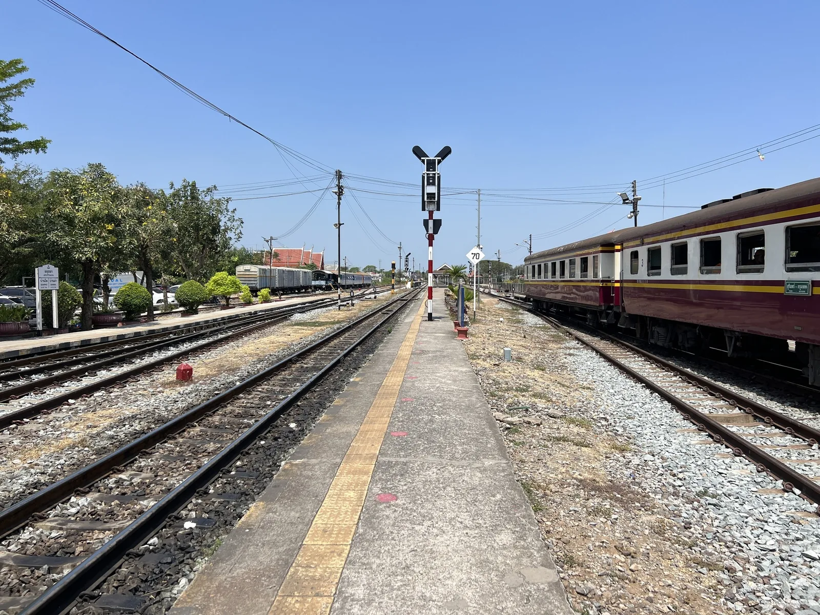 A maroon train carriage stands at a quiet platform lined with tracks and signal poles at Ayutthaya train station.