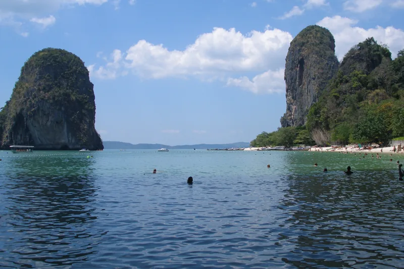 Swimmers enjoy calm turquoise water between limestone karsts at Railay Beach in Krabi, Thailand.