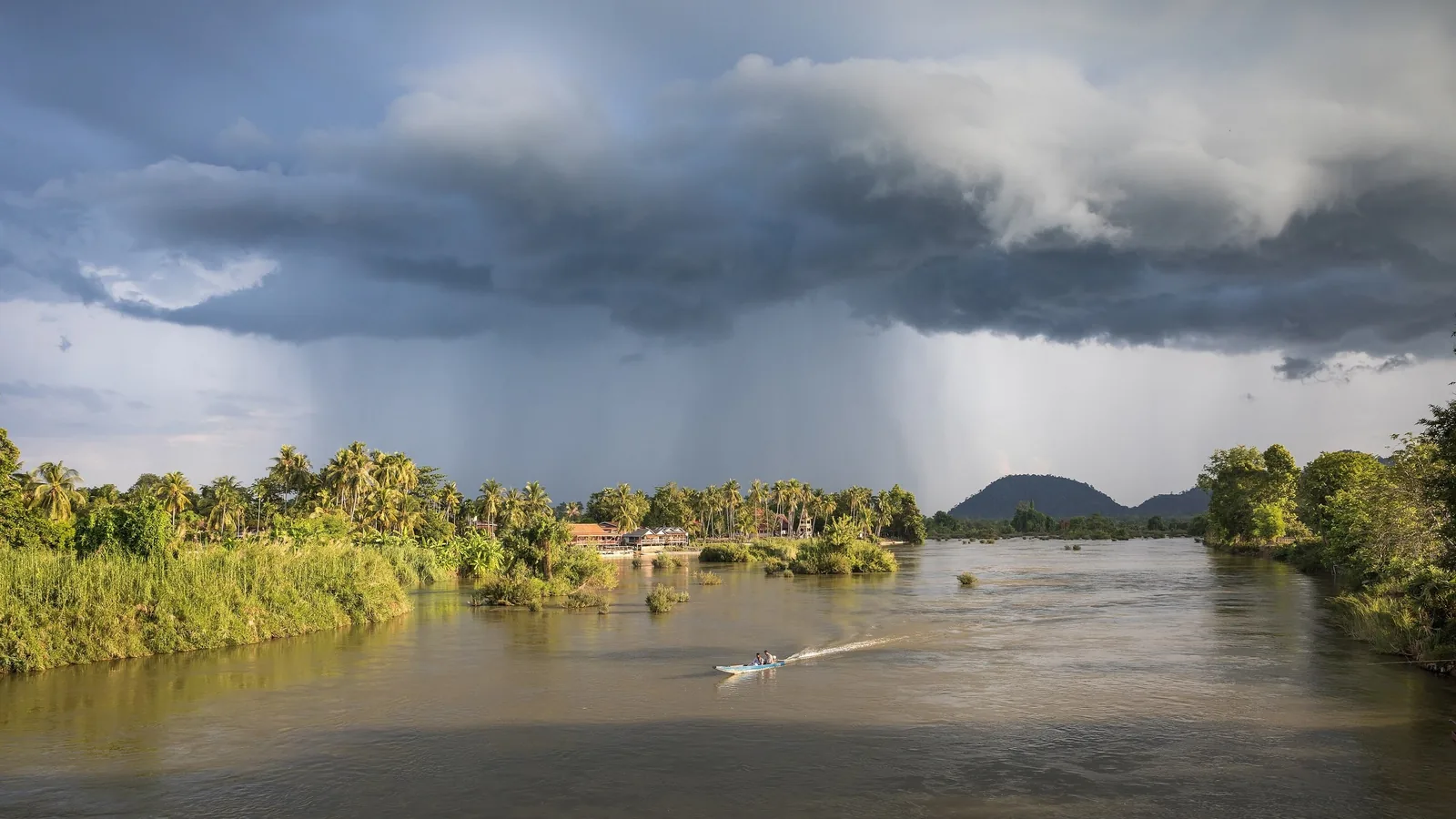 A small boat crosses the Mekong River under dramatic storm clouds in Si Phan Don, Laos.