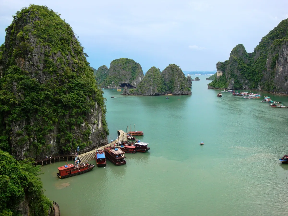 Wooden boats dock beside limestone karsts rising from the emerald waters of Ha Long Bay.