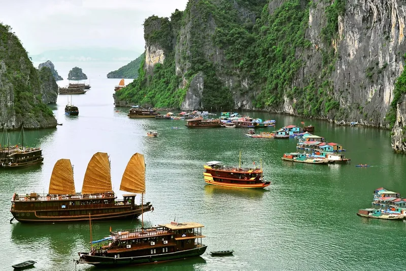Sail junks and a floating fishing village drift among limestone karsts in Ha Long Bay, Vietnam.
