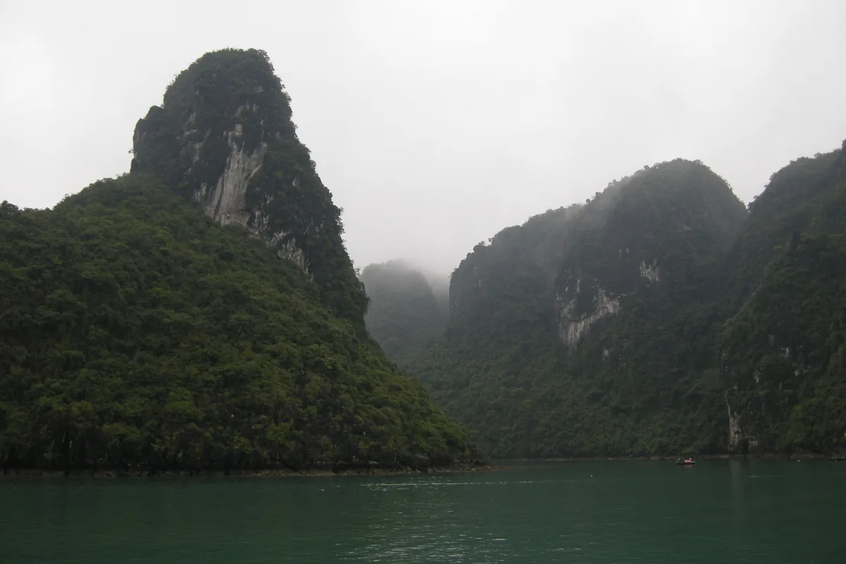 Misty limestone karst towers rise above green water in Ha Long Bay.