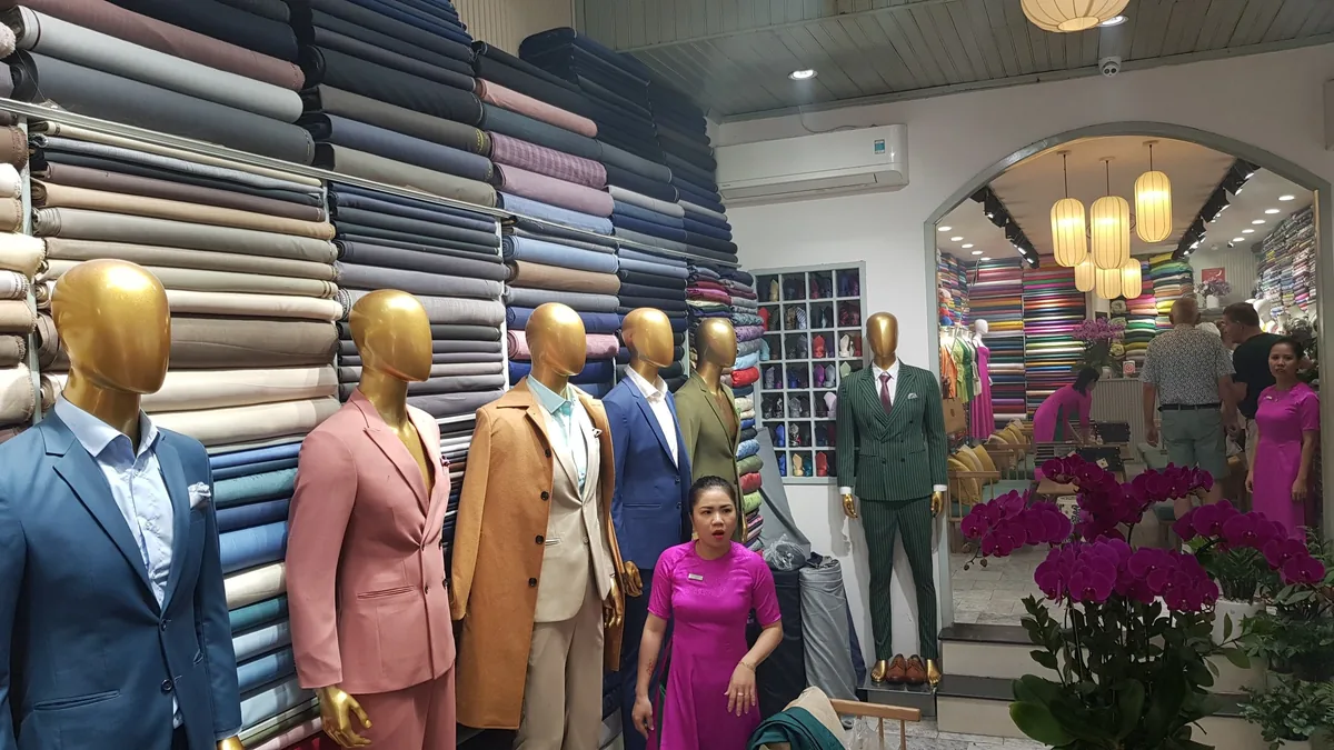 Mannequins in tailored suits and stacked fabric rolls fill a tailor shop in Hoi An.