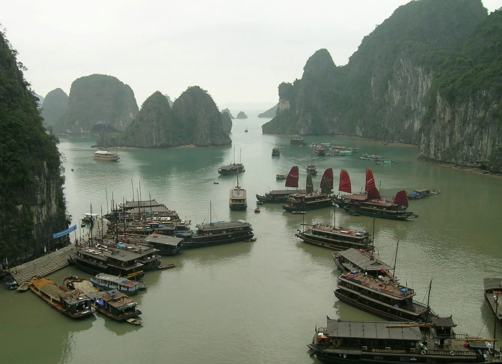 Wooden junks with red sails cluster among limestone karsts in Ha Long Bay.