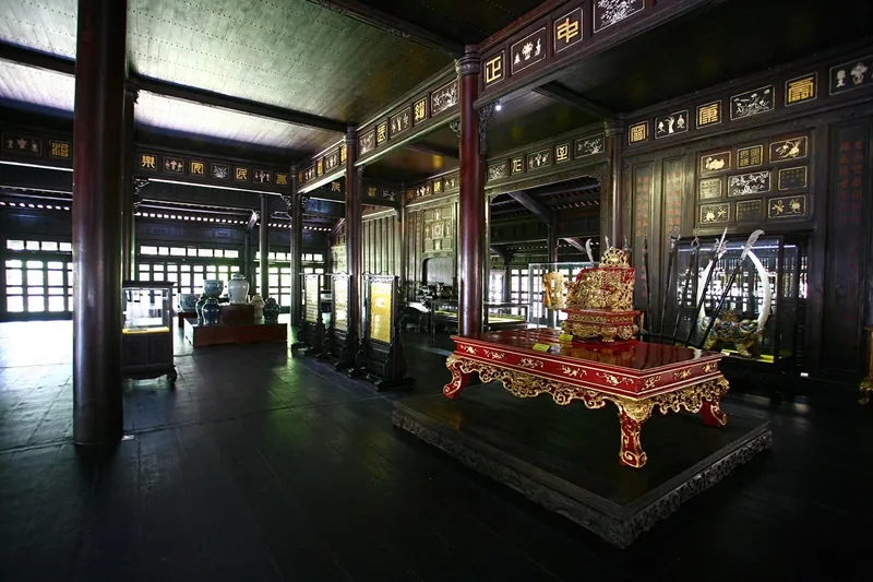 A gilded imperial throne sits inside a dark wooden hall decorated with lacquered panels in Hue.