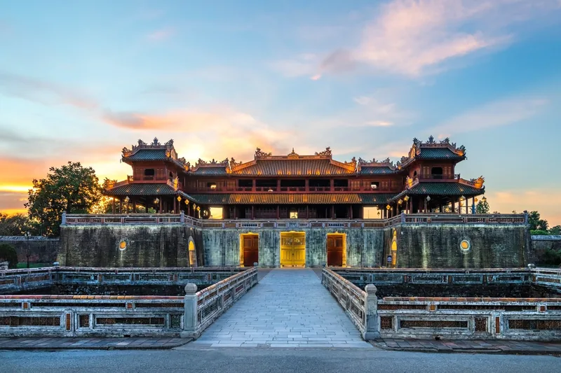 The Meridian Gate of Hue Imperial Citadel glows at sunset behind its stone bridge and moat.