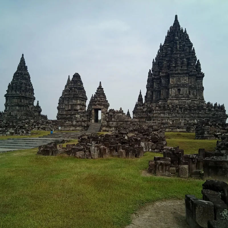 Towering stone spires of Prambanan temple complex rise above scattered ruins and grass in Yogyakarta.