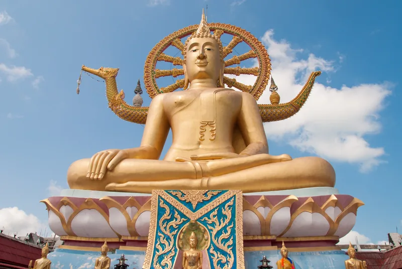 A giant golden seated Buddha statue rises against a blue sky at the Big Buddha temple in Koh Samui.