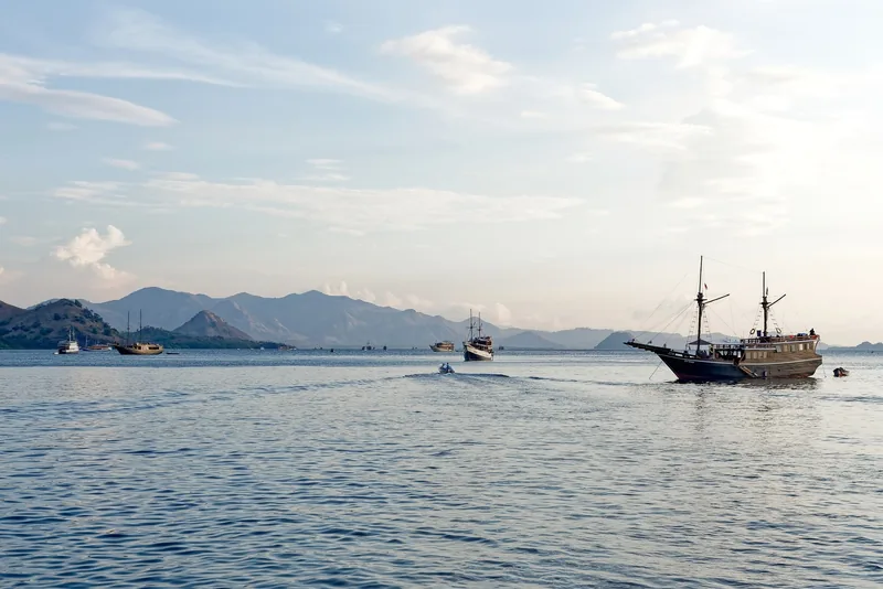 Wooden phinisi boats anchor on calm sea near hilly islands close to Labuan Bajo, Indonesia.
