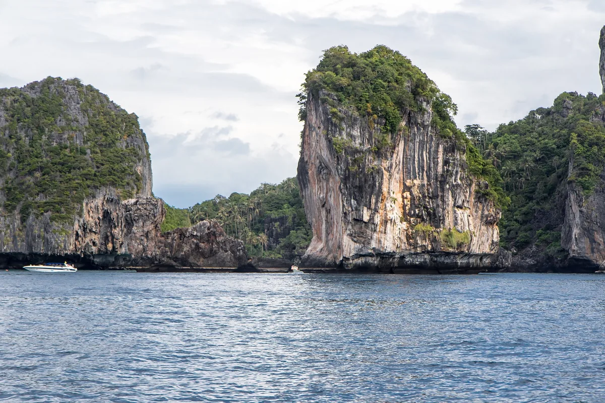 Limestone karst cliffs rise from turquoise sea near Krabi with a small boat passing by.