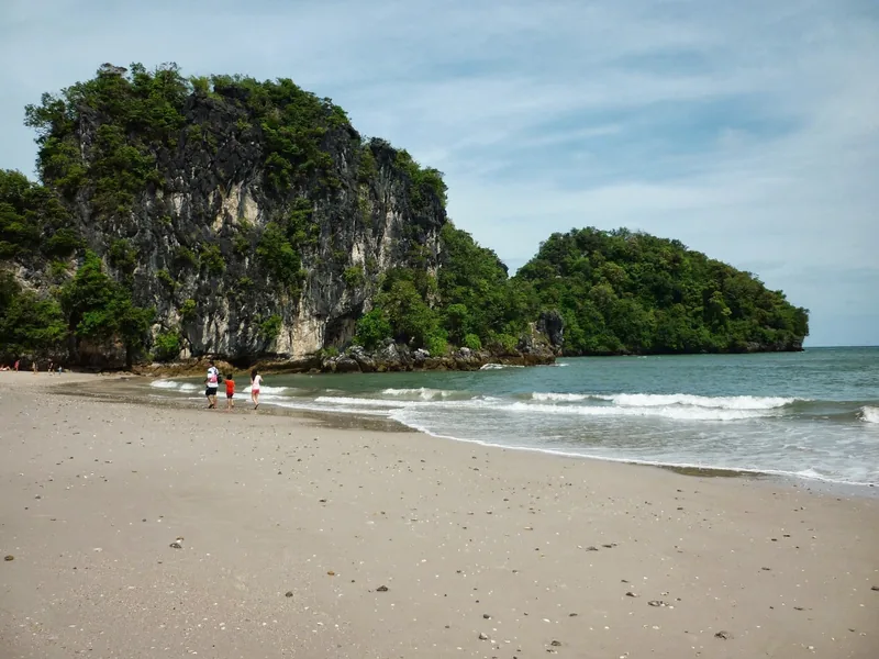 Limestone cliffs rise above a sandy beach as small waves roll in near Ao Nang, Krabi.