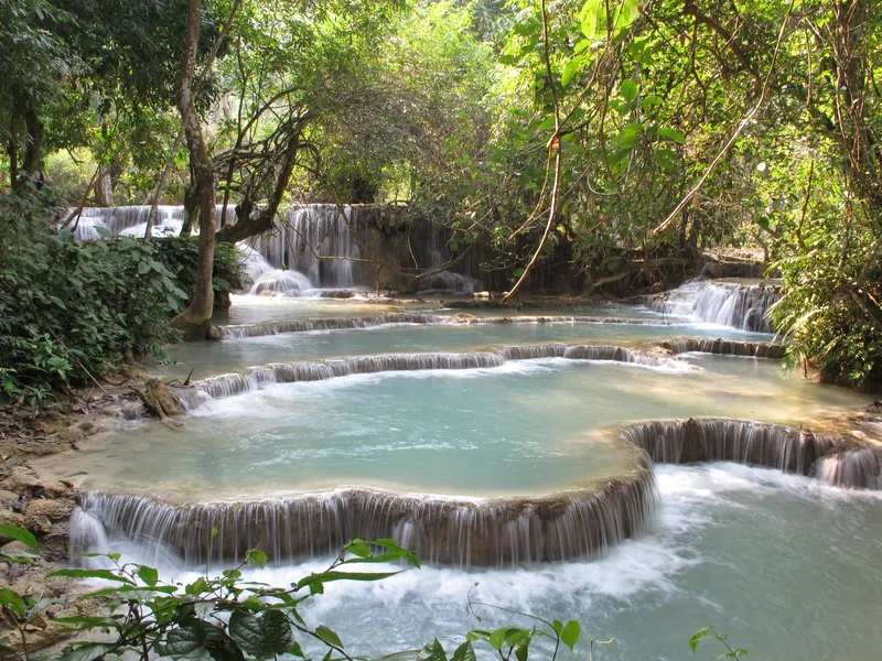 Turquoise cascading pools of Kuang Si Falls flow through lush jungle near Luang Prabang, Laos.