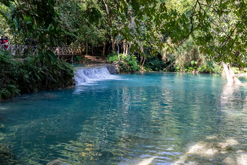 Turquoise pool and small cascade beneath a wooden bridge at Kuang Si Falls near Luang Prabang.