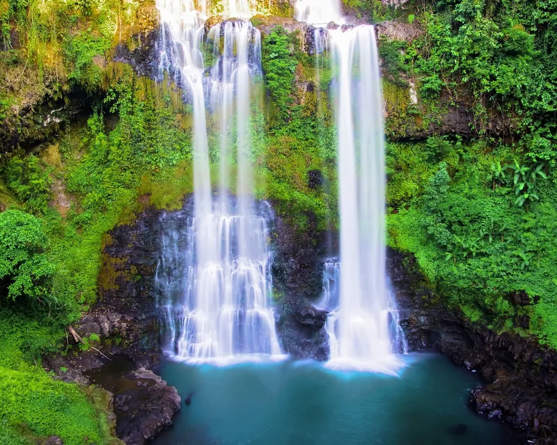 Twin cascades tumble over a mossy cliff into a turquoise pool on the Bolaven Plateau, Laos.