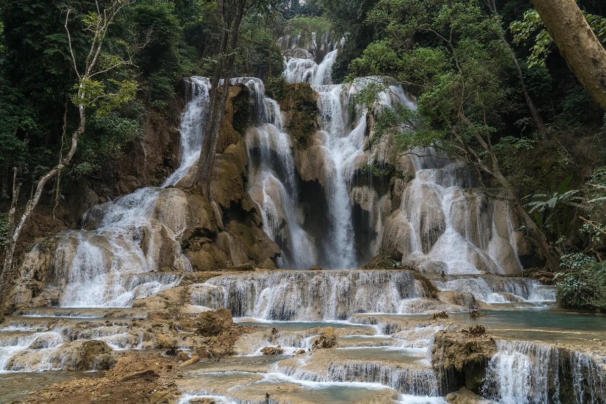 Multi-tiered limestone cascades of Kuang Si Falls flow over turquoise pools near Luang Prabang.