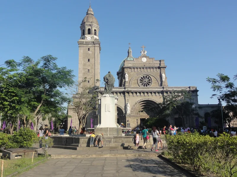 Visitors gather in front of Manila Cathedral's stone facade and bell tower in Intramuros.