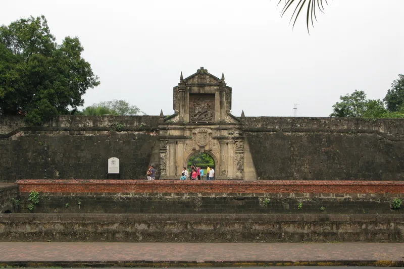 Visitors gather at the ornate stone gate of Fort Santiago within the walled city of Intramuros, Manila.