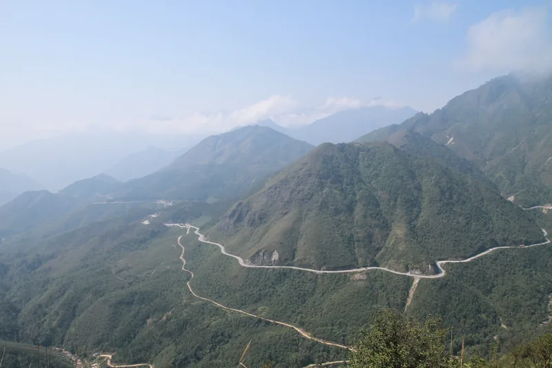 A winding mountain road snakes through green misty peaks near Sapa, Lao Cai.