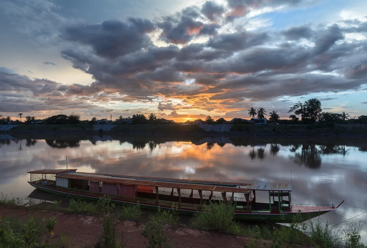 A wooden riverboat rests on the bank of the Mekong River at sunset near Pakse, Champasak.