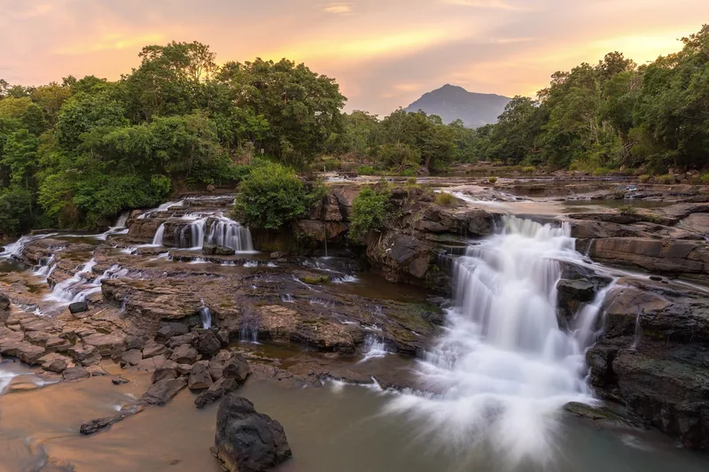 A tiered waterfall cascades over rocky ledges at sunset near Tad Lo village on the Bolaven Plateau, Laos.