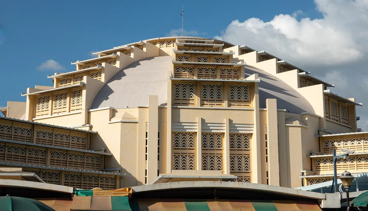 The art deco dome of Phsar Thmey (Central Market) rises above market stalls in Phnom Penh under a blue sky.