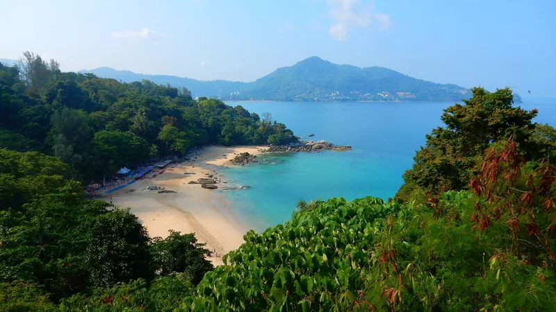 A lush green headland frames a secluded sandy beach and turquoise bay in Phuket.