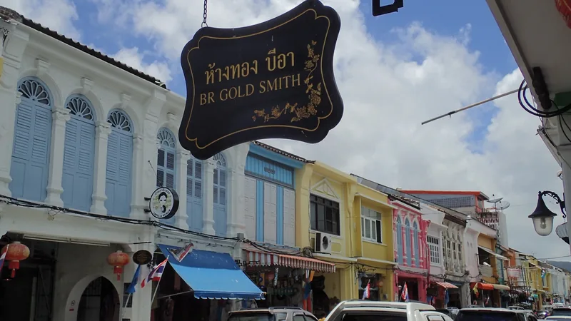 Colorful Sino-Portuguese shophouses line a street with a goldsmith shop sign in Phuket Town.